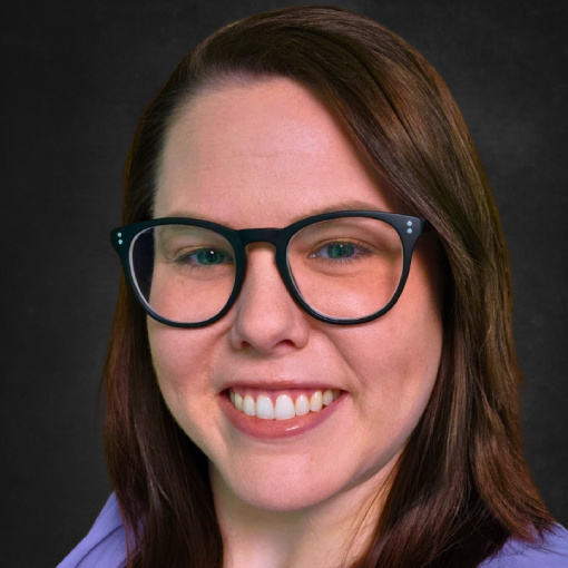 A woman with long brown hair, wearing dark-framed glasses and a purple top, smiles against a dark background.