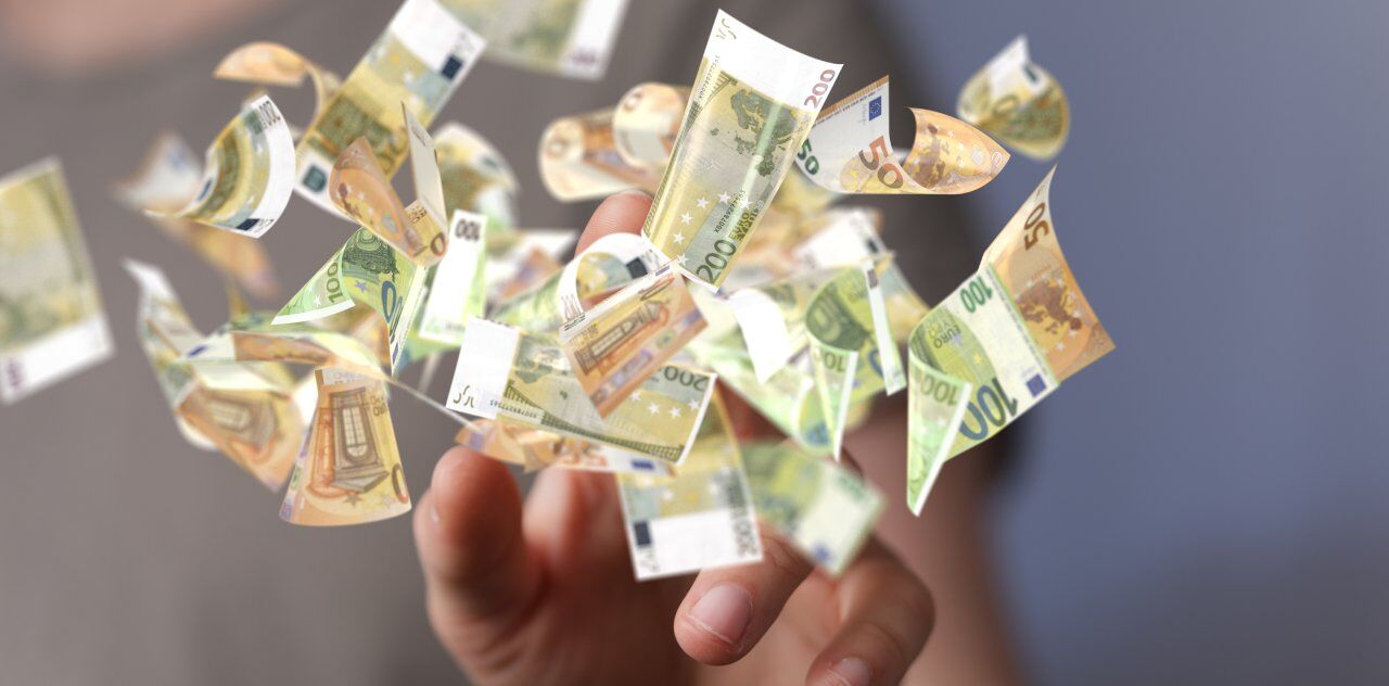A person reaching into the air as numerous euro banknotes, including 100 and 200 denominations, are scattered and floating around. The focus is on the swirling money, creating a dynamic and energetic scene.