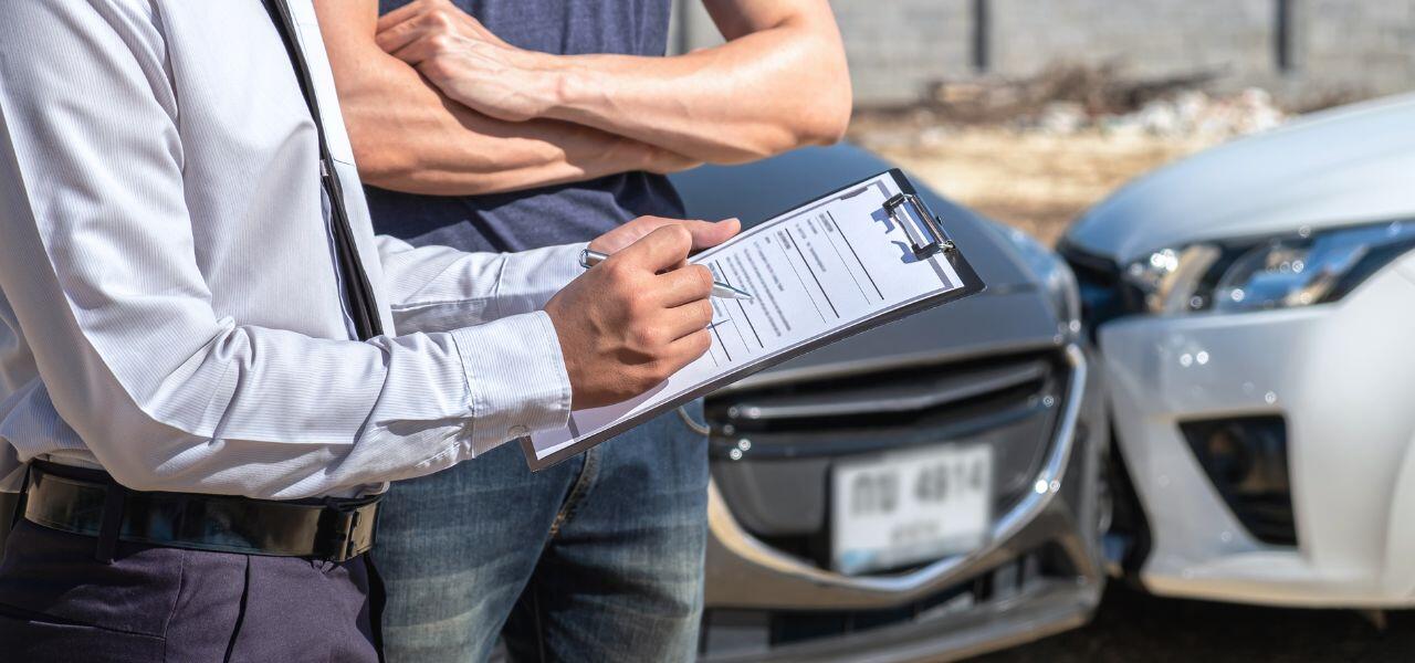 A person in a white shirt is holding a clipboard and pen, standing near two cars with minor frontal damage. Another person in casual attire stands with arms crossed. The scene appears to be an accident report assessment.