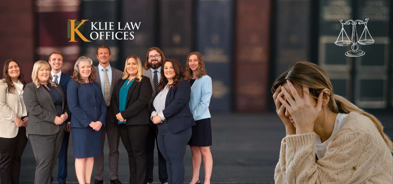 A group of nine professionally dressed individuals from Klie Law Offices stands together on the left, with a distressed woman holding her head in her hands on the right. A scales of justice graphic is in the top right corner.