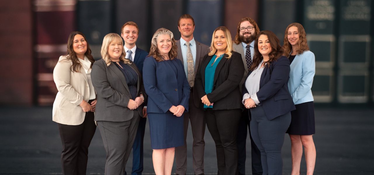 A group of ten people in professional attire standing together and smiling in front of a backdrop with large books.