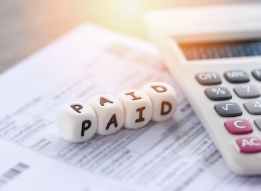 Close-up of a calculator on top of documents, with four dice spelling "PAID" in focus.