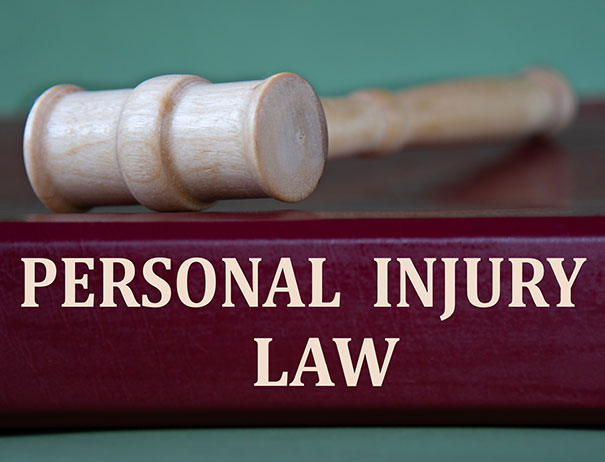 A wooden gavel rests on top of a maroon book titled "Personal Injury Law" with bold letters, set against a green background.