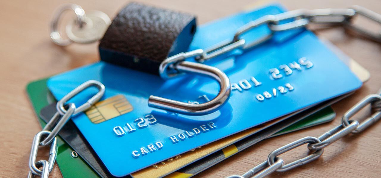 A stack of credit cards is secured with a chain and an open padlock. The chain is wrapped around the cards, symbolizing financial insecurity or vulnerability. The image focuses on the concept of credit card protection.