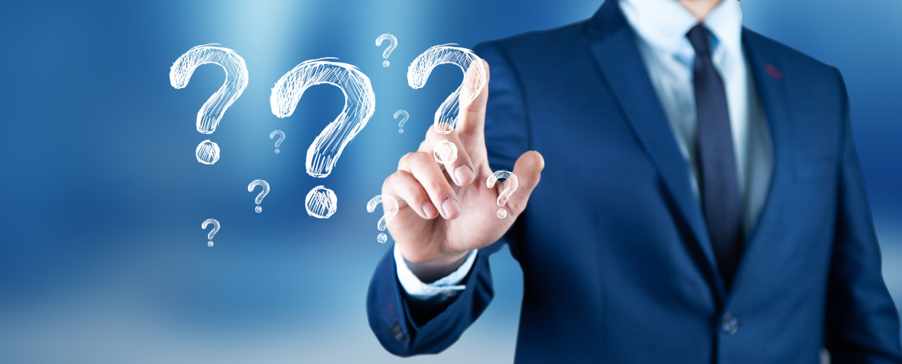 A person in a suit is standing against a blurred blue background, pointing at floating question marks. The image symbolizes curiosity or inquiry.