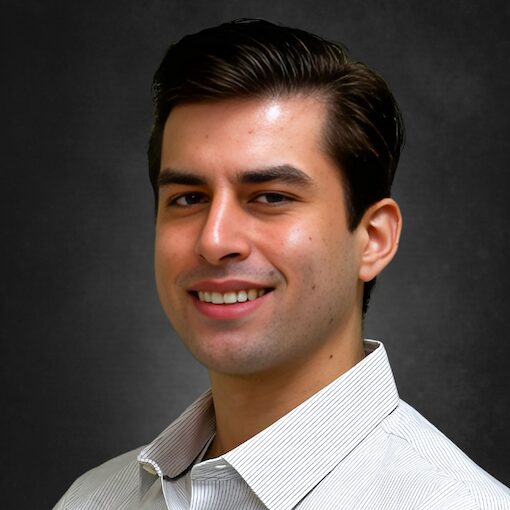 A man smiling, wearing a white collared shirt, posed against a dark gray background.