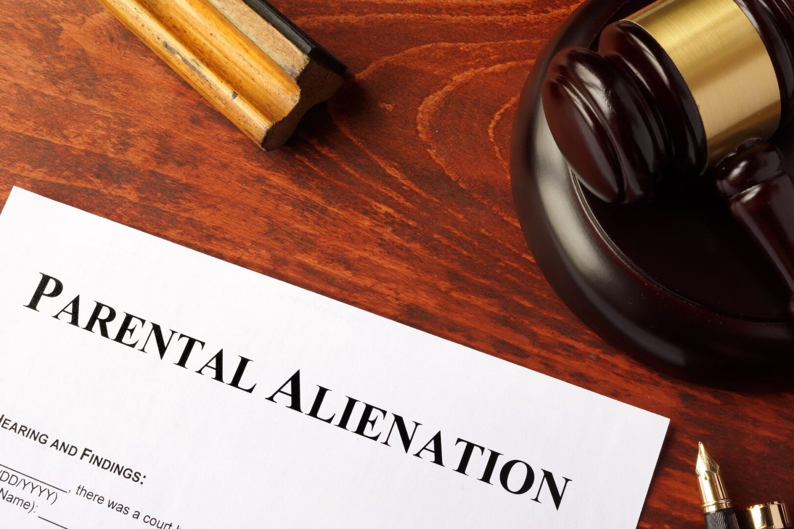 A wooden table with a gavel resting on it. In the foreground, there is a document titled "Parental Alienation" with a partially visible pen beside it.