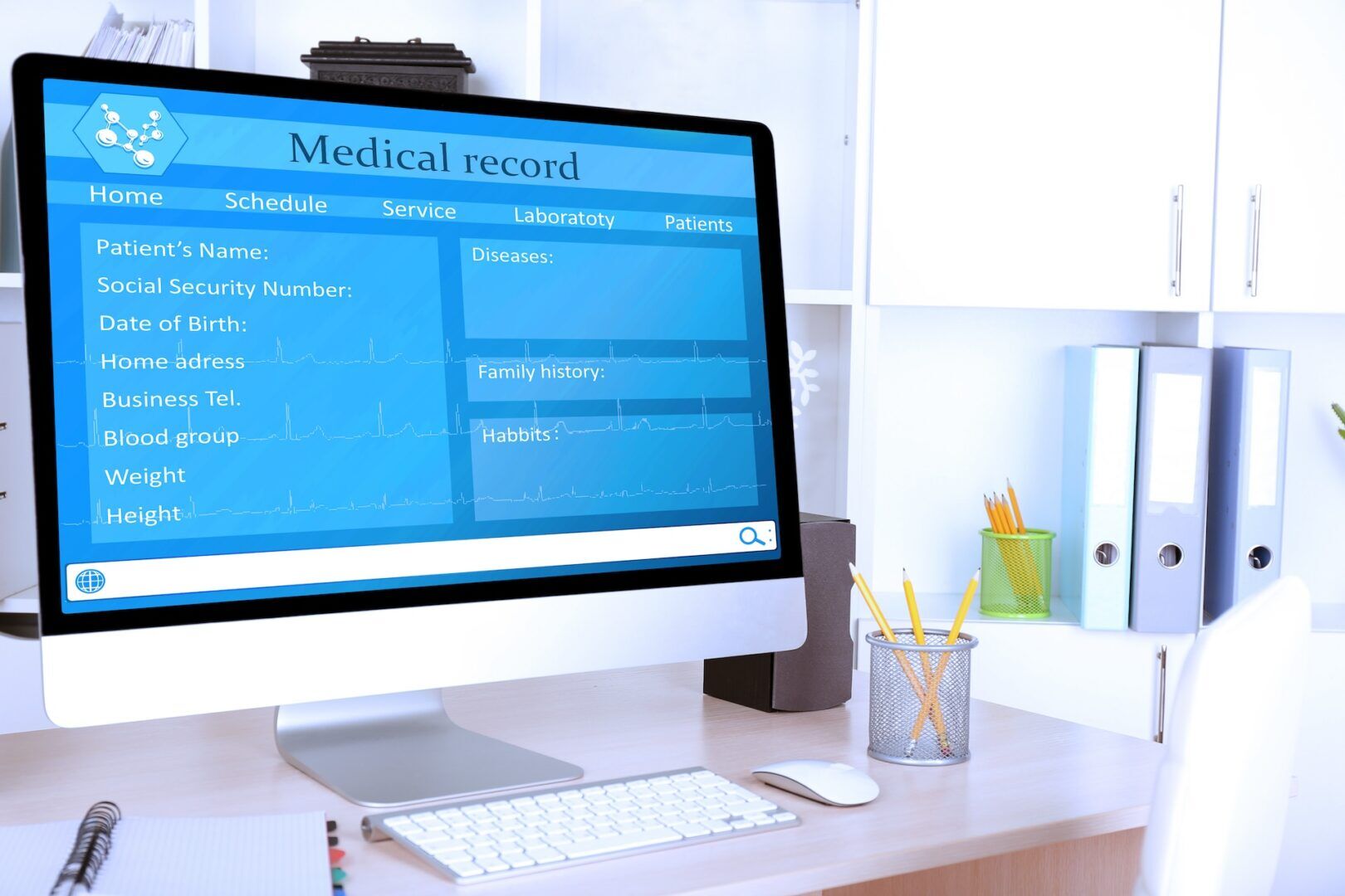A computer screen on a desk displays a medical record form, showing fields for patient's name, Social Security number, date of birth, address, and other personal information. The background includes a desk with office supplies and shelves.