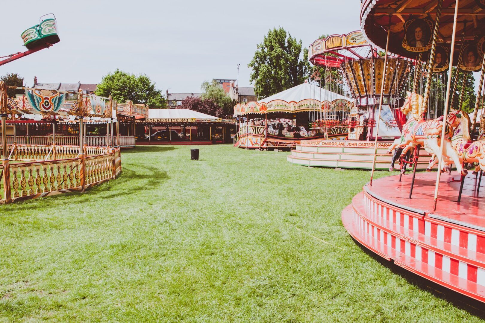 Vintage carousel rides on a grassy field with bright red and gold accents create the perfect spring break idea for divorced families. The sunny scene, dotted with trees and distant buildings, offers a nostalgic fairground setting where carousel horses invite joy and unity.