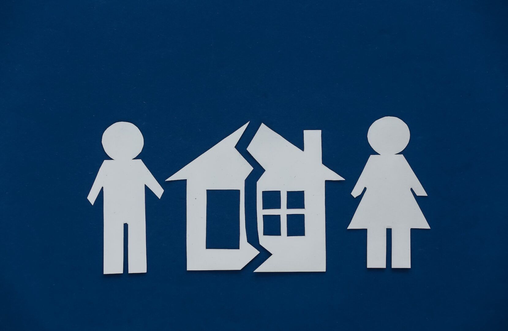 Paper cutouts of a man and a woman stand on either side of a house split in two, symbolizing separation or divorce. This scene evokes the question: What Is Necessary to File a Temporary Restraining Order in West Virginia?.