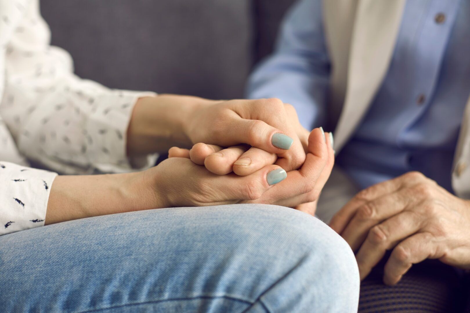 Two people sit closely together, one gently holding the hands of the other, offering comfort and support—just as understanding What Is the Difference Between Legal Separation and Divorce can provide reassurance in difficult times. Soft, natural light highlights their hands.