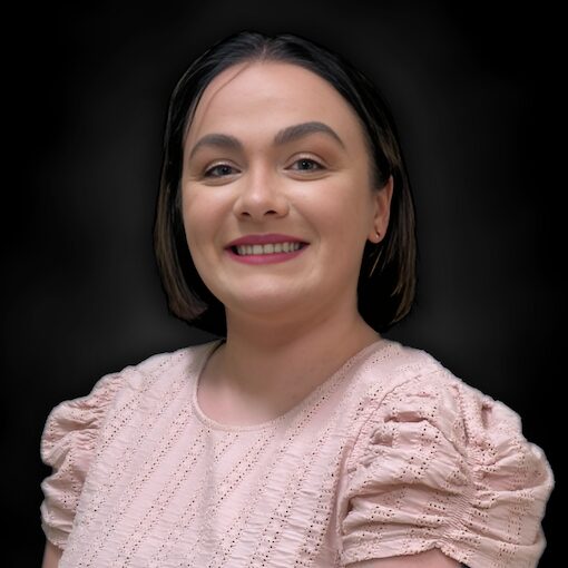 A woman with short dark hair, wearing a light pink textured blouse, smiles confidently against a black background.