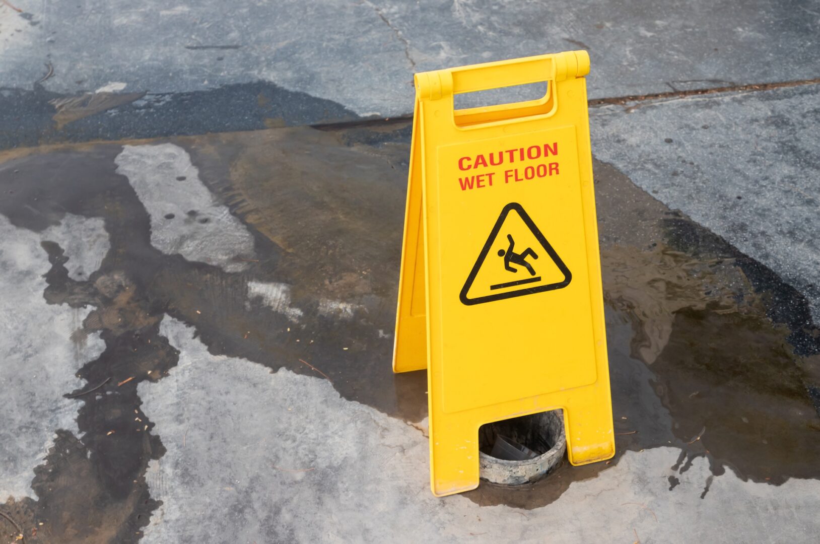 A yellow "Caution Wet Floor" sign stands on a concrete surface next to a puddle of water, much like a guide to asset division in divorce warns couples of potential pitfalls during the separation process.