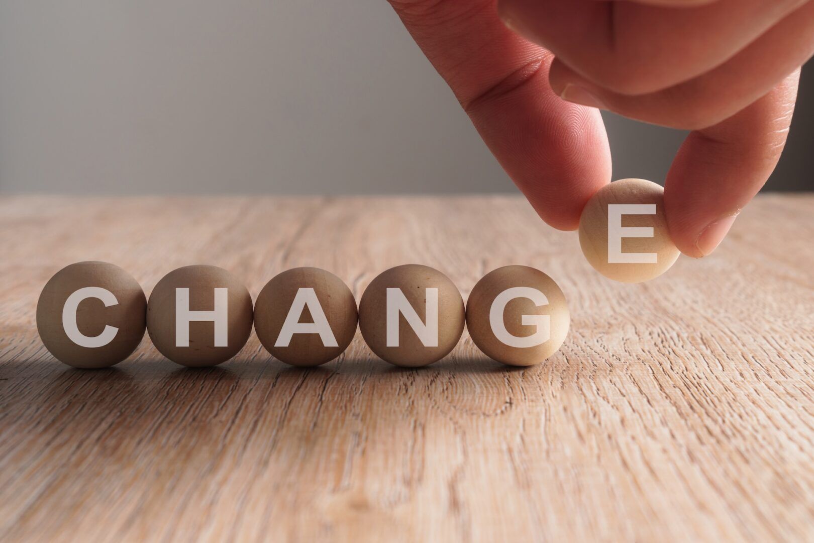 A hand is placing a wooden ball with the letter "E" at the end of a row spelling "CHANGE" on a wooden surface, symbolizing transformation—much like understanding How is Alimony Calculated in West Virginia can bring about progress during life changes.