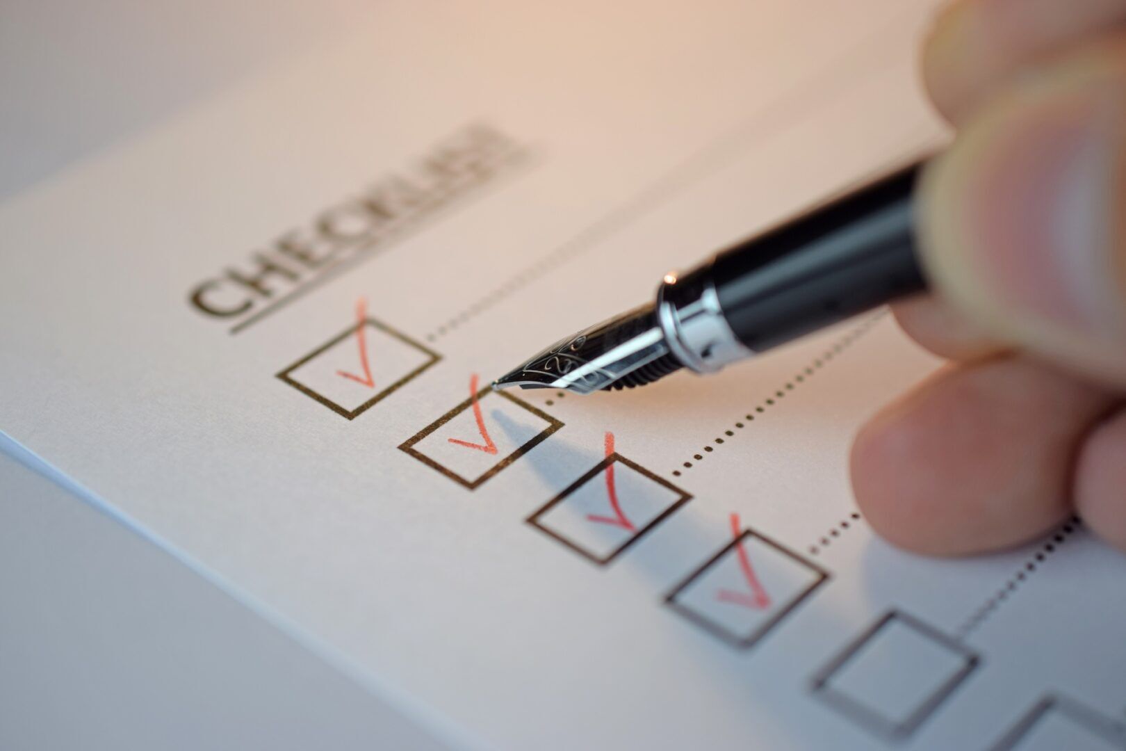A close-up of a hand holding a fountain pen, checking off boxes on The Essential Evidence Checklist for Personal Injury Cases. Several boxes are already marked with bold red check marks.
