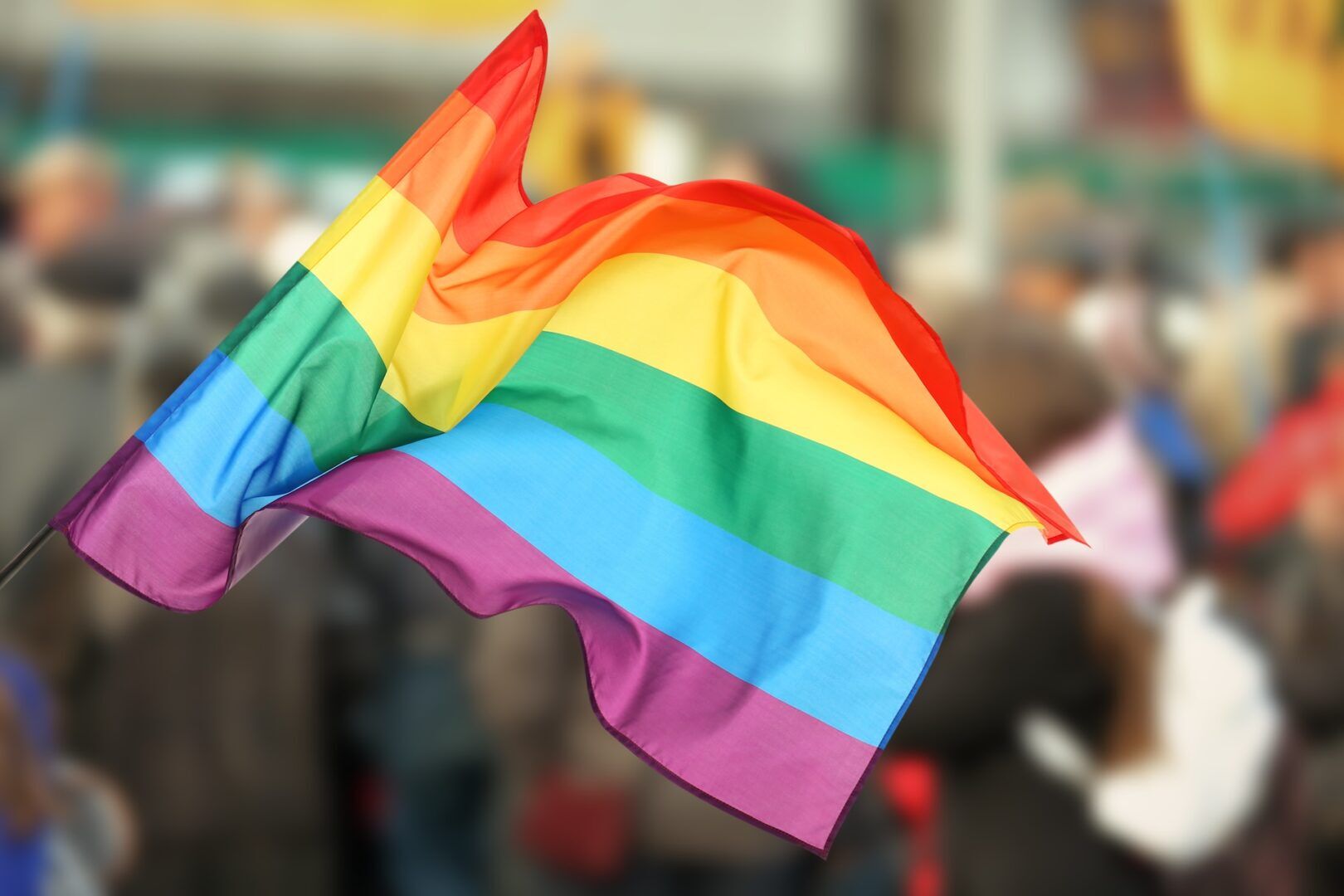 A rainbow-colored pride flag waves prominently, with blurred people and buildings in the background, symbolizing LGBTQ+ pride and diversity—reminding us to know when to call an attorney if you face situations where what injuries require a personal injury lawyer.