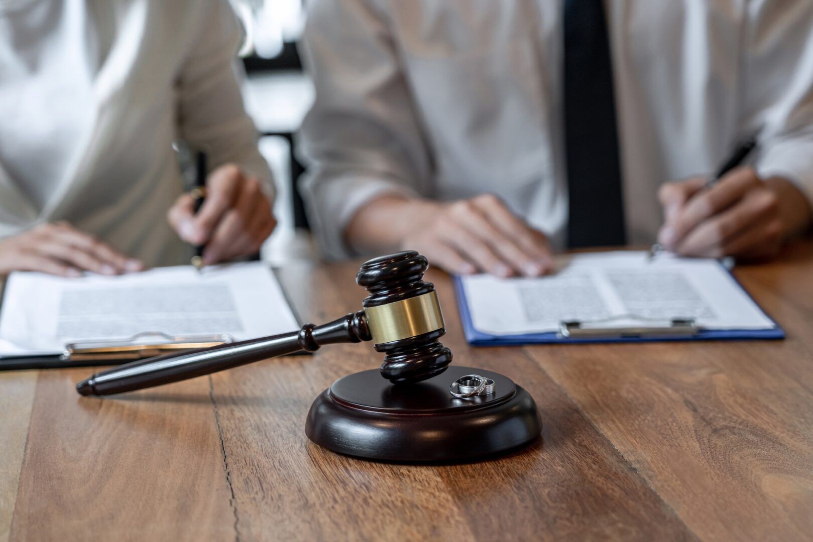 A judge's gavel and a pair of wedding rings rest on a wooden table, as two people in formal attire sign documents—symbolizing key decisions like those faced when learning How to Recognize and Respond to Workplace Discrimination in West Virginia.
