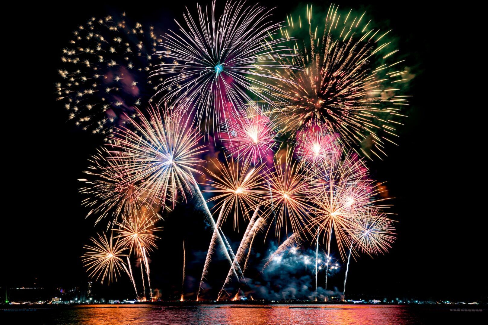 Colorful fireworks burst in the night sky over water, reminiscent of Fireworks & Fair Time: Tips for Child Custody Over Summer Holidays, as bright reflections illuminate the scene with vibrant reds, blues, purples, and yellows.