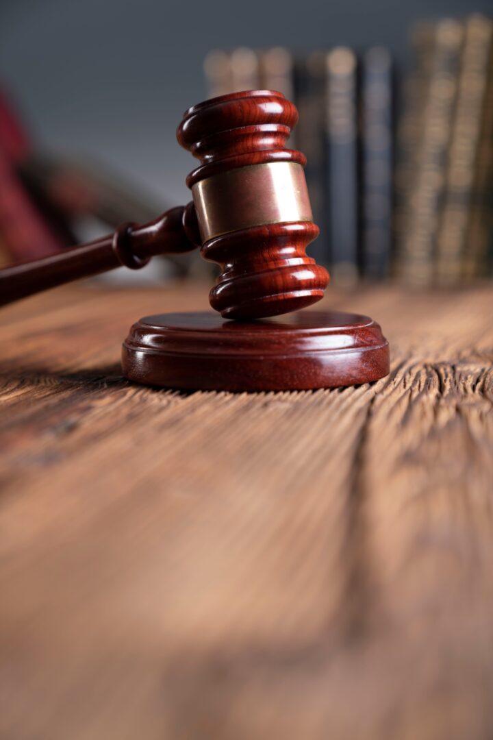 A wooden judge’s gavel rests on a sound block atop a rustic wooden table, with blurred law books in the background. A wooden judge’s gavel rests on a sound block atop a rustic wooden table, with blurred law books in the background.