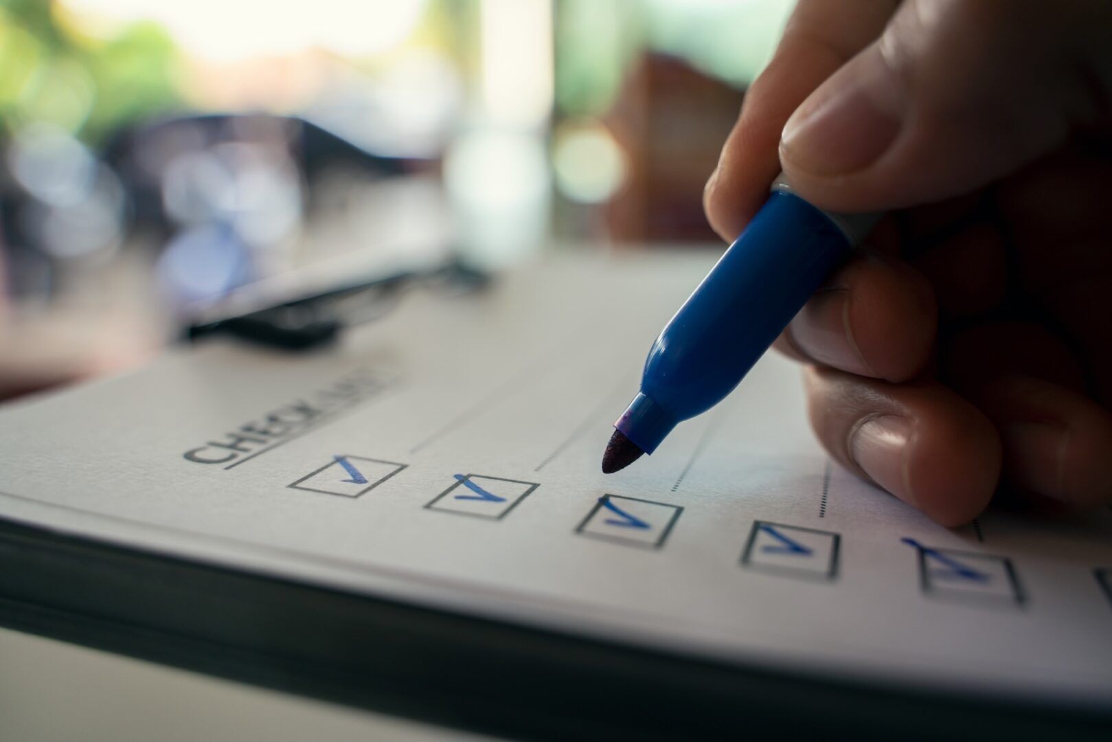 Close-up of a hand with a blue marker checking off boxes on a printed checklist, representing steps in understanding how to use West Virginia's two-year personal injury statute of limitations. A row of blue checkmarks lines the form, with blurred background elements.