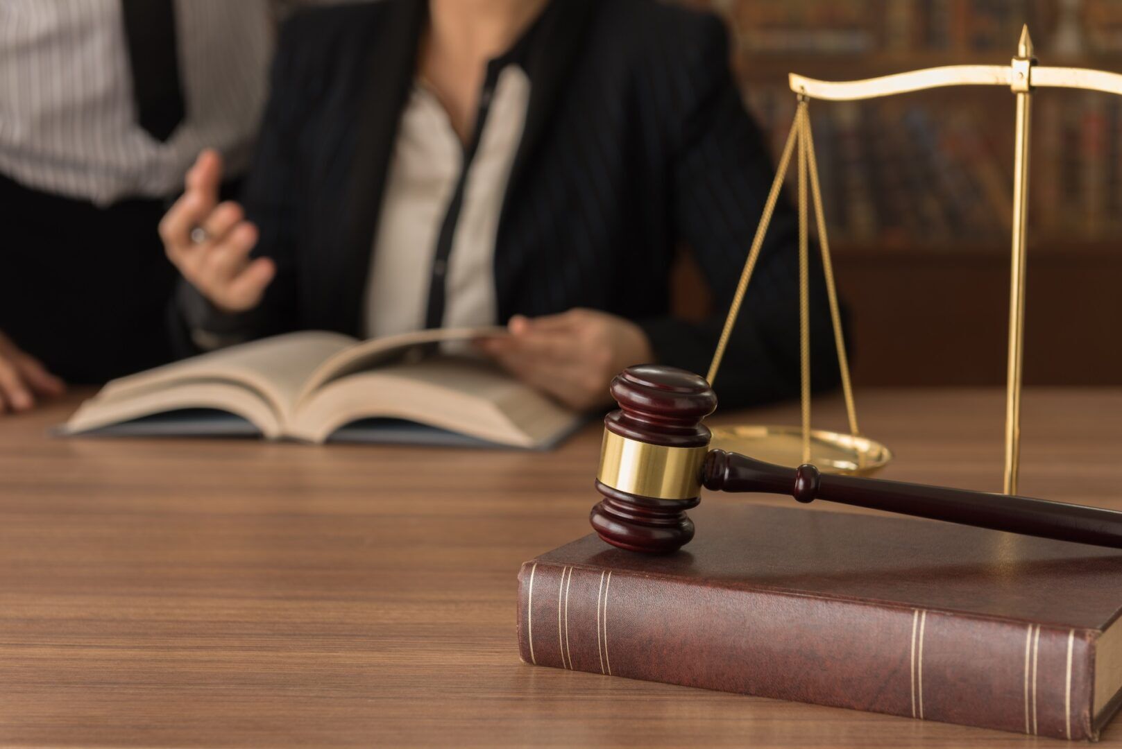 A gavel rests on a law book beside scales of justice, as two people in business attire discuss how to use West Virginia's two-year personal injury statute of limitations while reviewing an open book in the background.