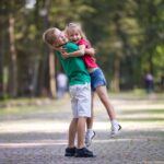 A young boy and girl hug and smile joyfully in a tree-lined park, with the boy lifting the girl off the ground. Much like learning how to use West Virginia's two-year personal injury statute of limitations, this moment captures the value of time.