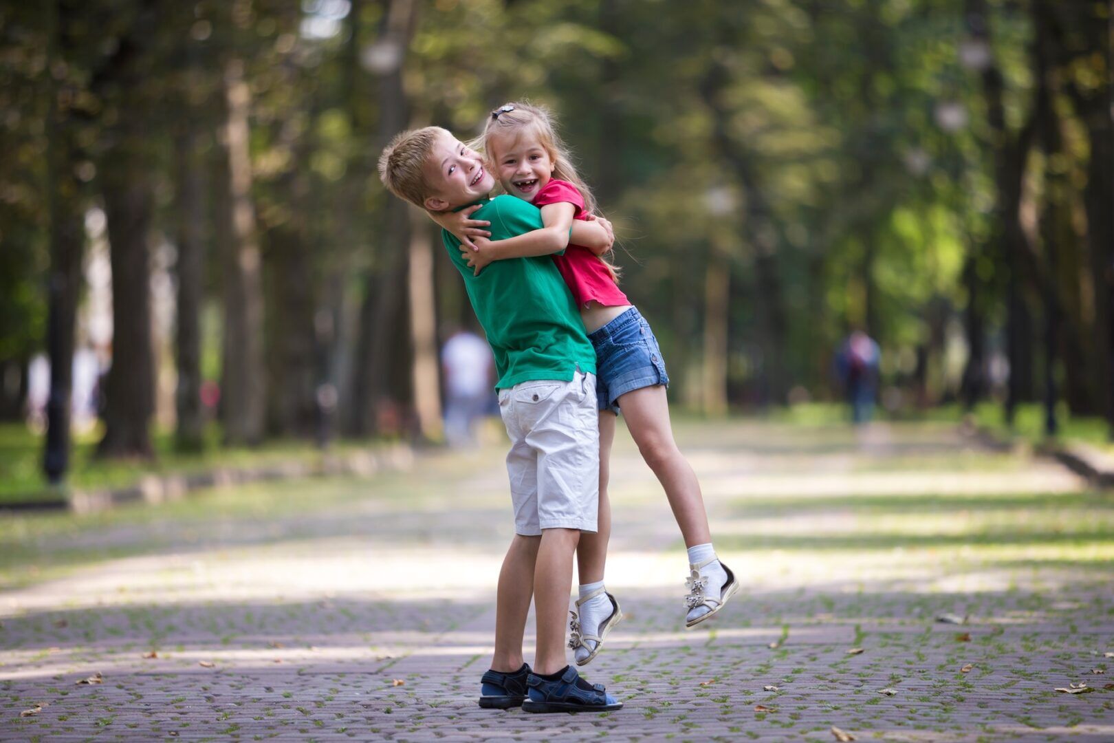A young boy and girl hug and smile joyfully in a tree-lined park, with the boy lifting the girl off the ground. Much like learning how to use West Virginia's two-year personal injury statute of limitations, this moment captures the value of time.