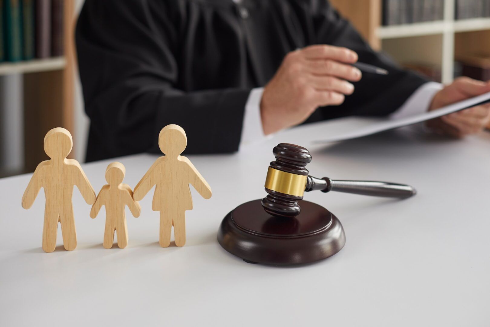 A judge in a black robe sits at a desk holding papers, with wooden family figures and a gavel in the foreground, symbolizing how courts decide custody and what factors WV courts consider in child custody cases.