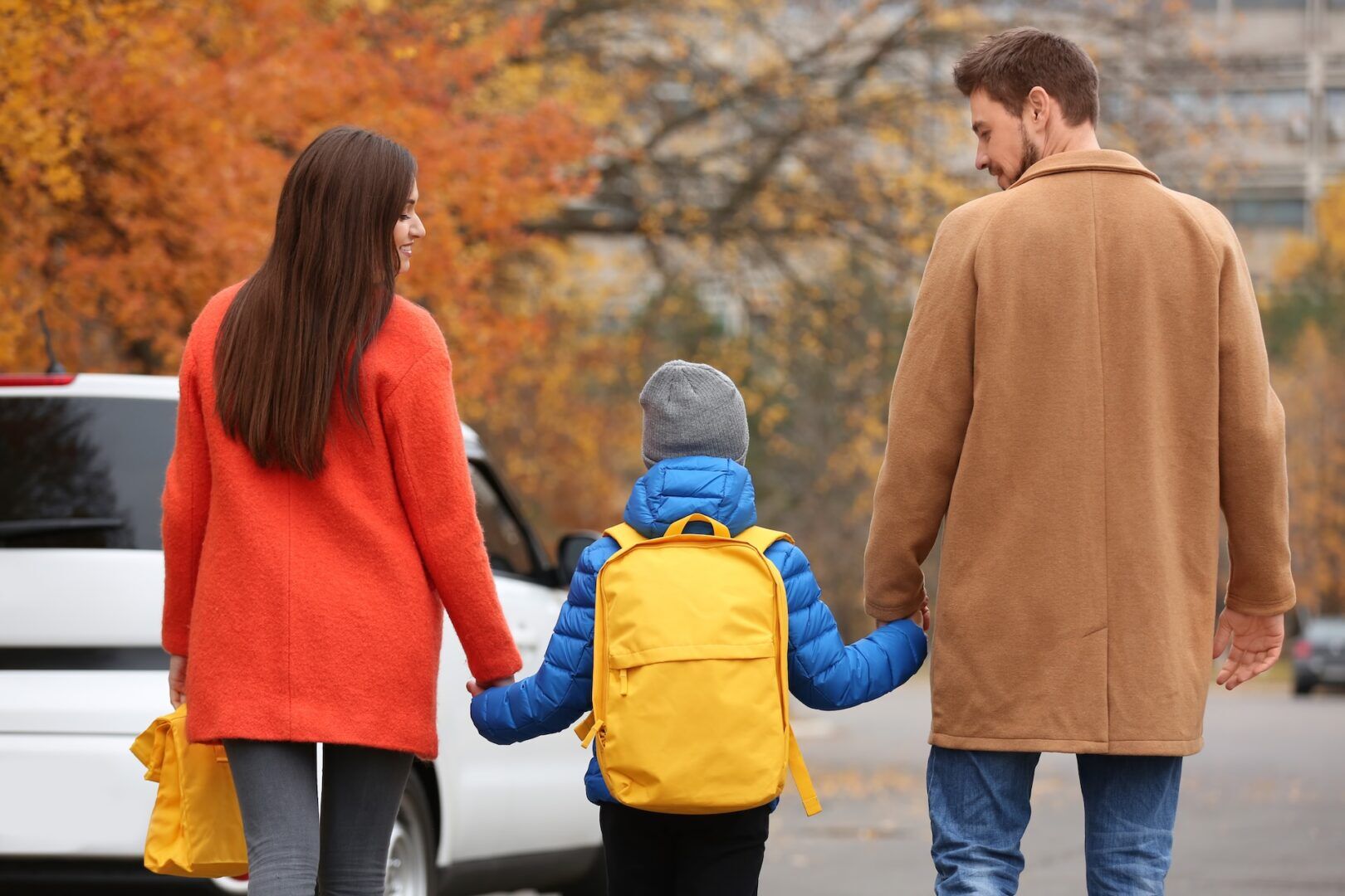 A family walks hand in hand down a tree-lined street in autumn, reflecting shared parenting.