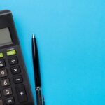 A black calculator and a black pen, perfect for Ohio child support calculations 2026, are placed side by side on a bright blue background, with ample empty space on the right.