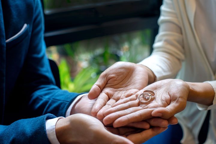 Close-up of two people’s hands, one person holding two wedding rings in their palm while the other gently supports their hand, suggesting an emotional or significant moment.