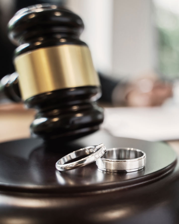 Two wedding rings rest on a judge’s gavel in a courtroom setting, symbolizing legal issues related to marriage or divorce.