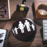 A wooden desk with a gavel, magnifying glass, keyboard, pen, notebook, glasses, and a round plaque showing a family icon—symbolizing how Ohio best interest child custody factors put families first.