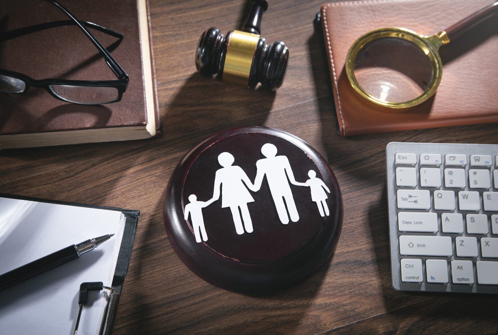A wooden desk with a gavel, magnifying glass, keyboard, pen, notebook, glasses, and a round plaque showing a family icon—symbolizing how Ohio best interest child custody factors put families first.