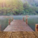 A wooden dock extends over a calm lake, surrounded by blurry trees in the background. The peaceful, misty atmosphere suggests a perfect spot to reflect on summer custody schedules amid nature’s quiet embrace.