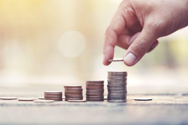 A hand stacking coins on one of several increasing piles of coins, symbolizing saving money and financial growth, with a soft, blurred background.