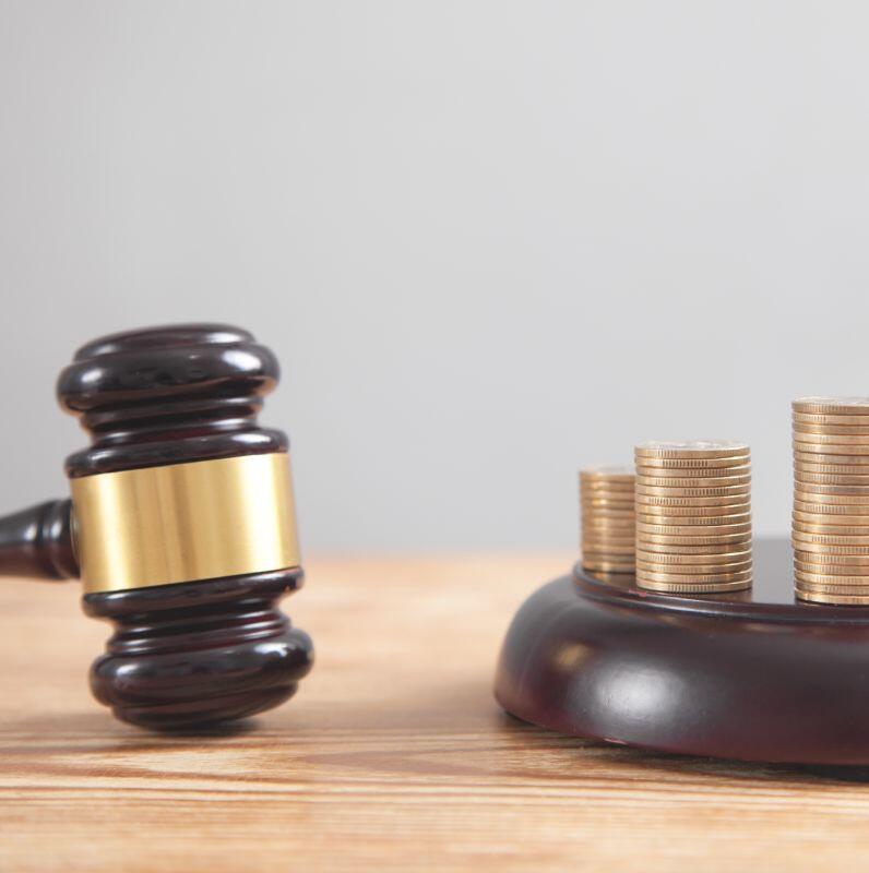 A judge's gavel lies next to a wooden base holding several stacks of gold coins, symbolizing law, justice, and financial matters.