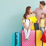 A smiling family of four sits on colorful suitcases against a light blue background. The parents and two children look at each other, appearing happy and ready for travel. The daughter holds a red backpack.