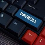 A computer keyboard with a large blue key labeled "PAYROLL" replacing the usual key, surrounded by black and red keys.