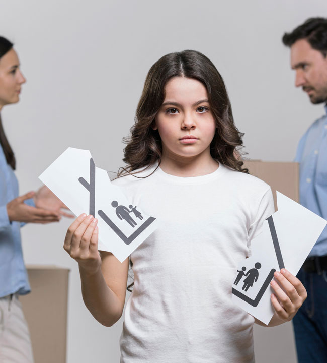 A sad girl holds two torn pieces of paper with family icons, while a man and woman argue in the background, symbolizing family separation or divorce.