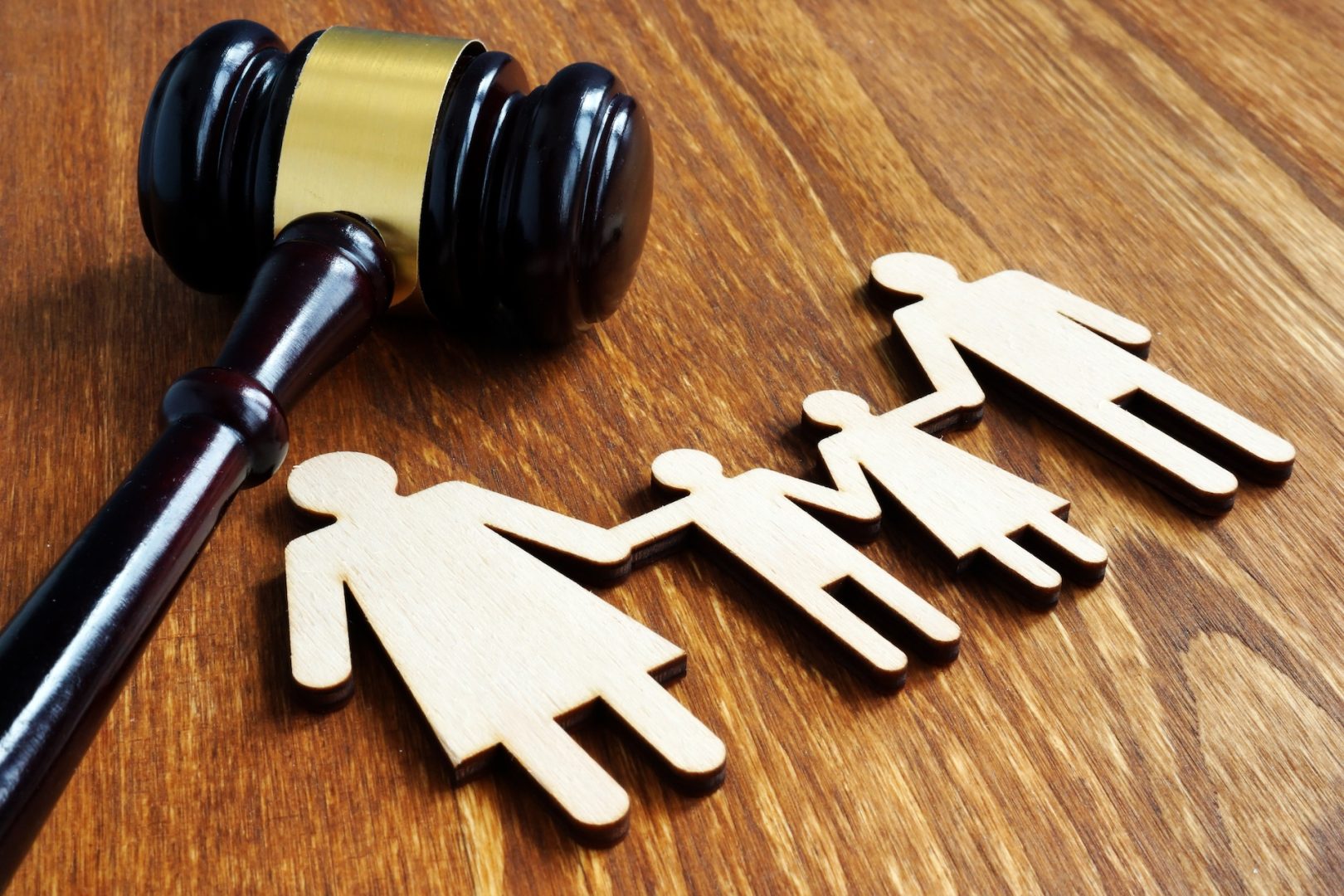 A judge's gavel lies next to wooden cutouts of two adults and two children holding hands, symbolizing family law or legal decisions affecting families.
