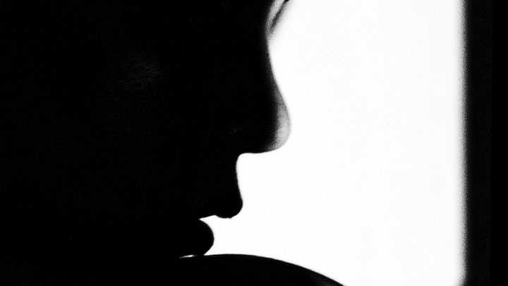 A close-up, black and white silhouette of a person's face in profile, highlighting the nose, lips, and chin against a bright white background.
