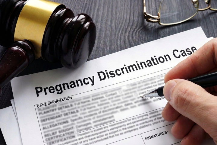 A person fills out a "Pregnancy Discrimination Case" form on a desk with a gavel, eyeglasses, and pen visible, suggesting a legal or workplace rights context.
