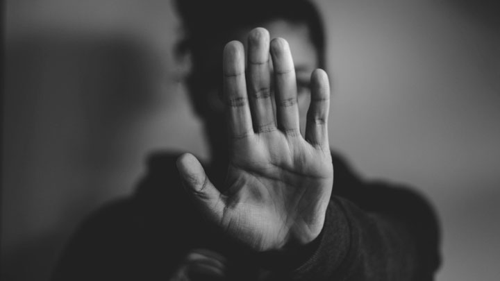 A person holding up their hand with the palm facing the camera, as if signaling to stop. The background is blurred and the image is in black and white.