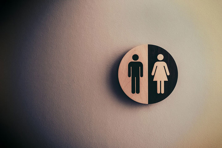 A round restroom sign on a wall, featuring half a male figure and half a female figure, divided vertically, symbolizing a unisex or gender-neutral bathroom.