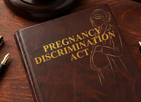 A brown book titled "Pregnancy Discrimination Act" with a gold outline of a pregnant woman on the cover, lying on a wooden desk alongside a pen and part of a gavel, represents one of the key Employment Law Practice Areas.