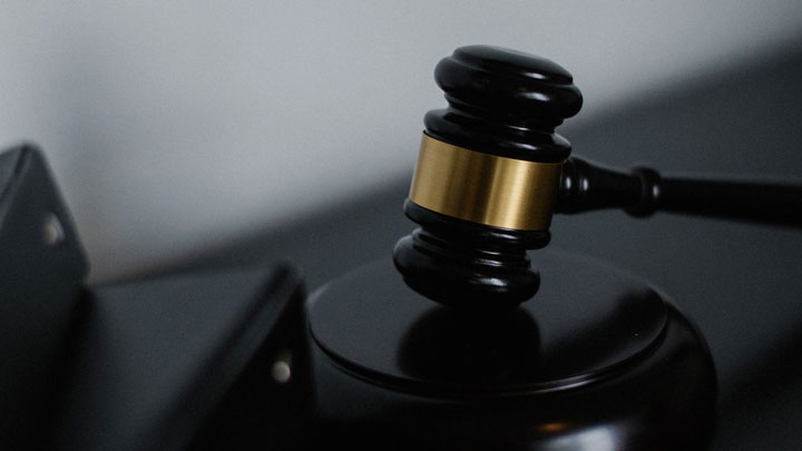 A close-up of a judge’s gavel resting on a sounding block, symbolizing law and justice, with a blurred black and gold background.