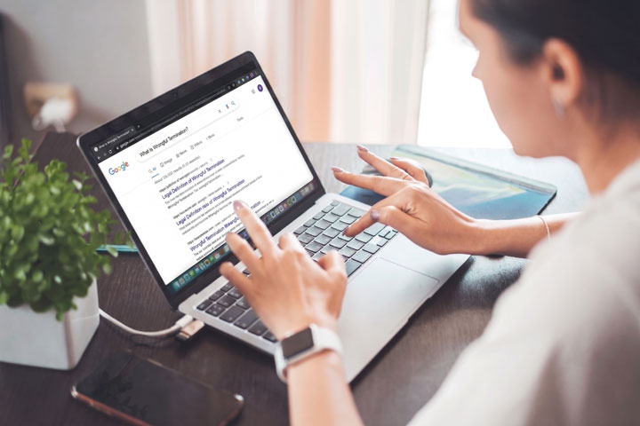 A person using a laptop at a desk, searching “What is digital marketing?” on Google. A smartphone, a plant, and a closed notebook are next to the laptop. The person wears a smartwatch.