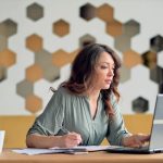 Parent using a laptop at a home desk with paperwork