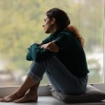 Woman sitting alone by a window looking thoughtful